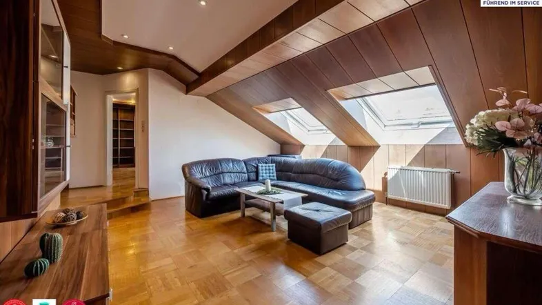 Gemütliches Wohnzimmer im Dachgeschoss mit Holzbalken, Parkettboden und Dachfenstern, die viel Licht hereinlassen.