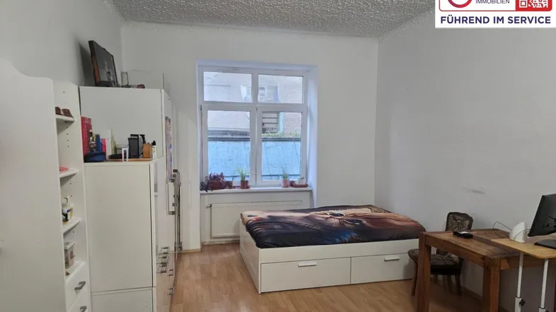 Helles Schlafzimmer mit Parkettboden, einem Bett mit Stauraum und einem Schreibtisch am Fenster.
