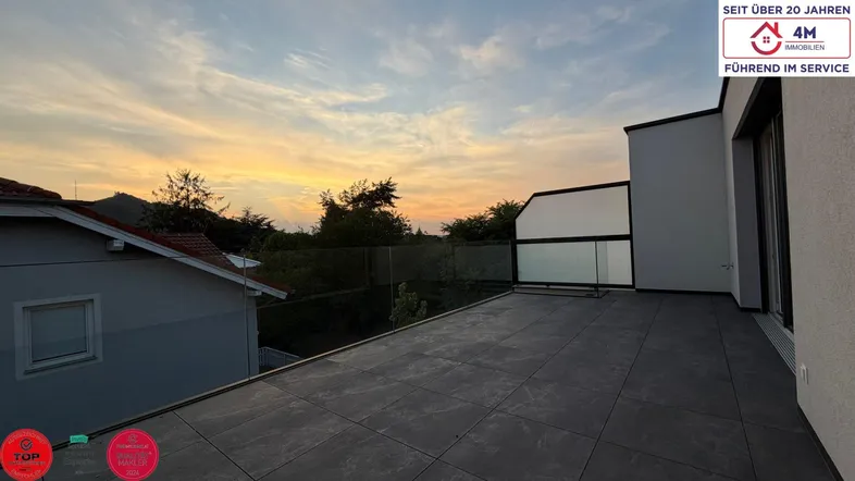 Große Dachterrasse mit Fliesenboden und Glasgeländer, ideal für entspannte Abende im Freien.