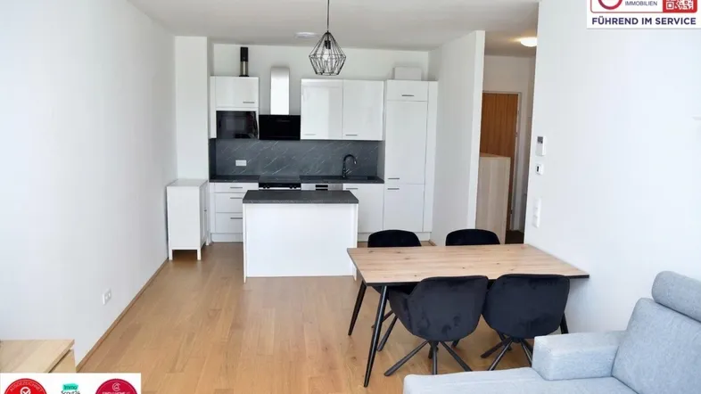Heller offener Wohn-Essbereich mit moderner weißer Küche und Holzboden, ideal für geselliges Beisammensein.