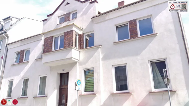 Weißes Mehrfamilienhaus mit traditioneller Architektur und Ziegelakzenten an den Fenstern.