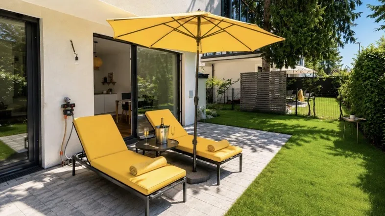 Geräumige Terrasse mit Sonnenliegen und Sonnenschirm, umgeben von einem gepflegten Rasen und Bäumen.