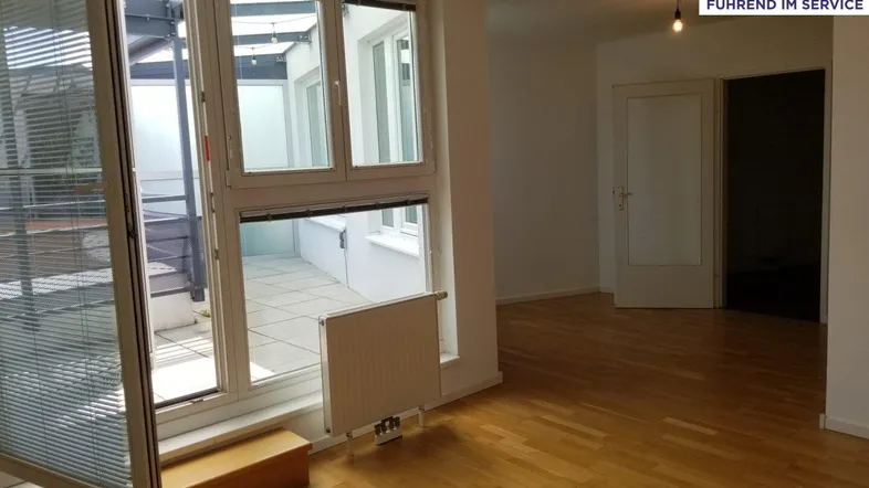 Heller Wohnraum mit Parkettboden und großen Fenstern, die Zugang zu einer Terrasse bieten.