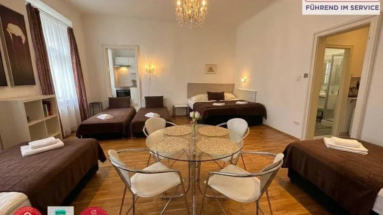 Geräumiges Wohnzimmer mit mehreren Betten, Esstisch und Kronleuchter, ideal für Gäste.