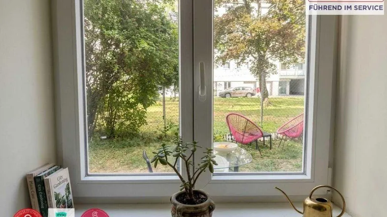 Blick aus einem Fenster auf einen begrünten Innenhof mit Sitzgelegenheiten und Pflanzen.