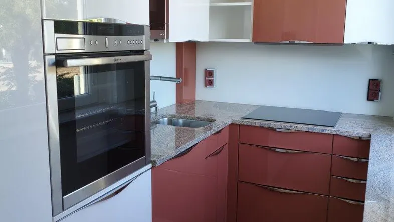 Stilvolle Küche mit integriertem Backofen, roten und weißen Hochglanzfronten und Granitarbeitsplatte.