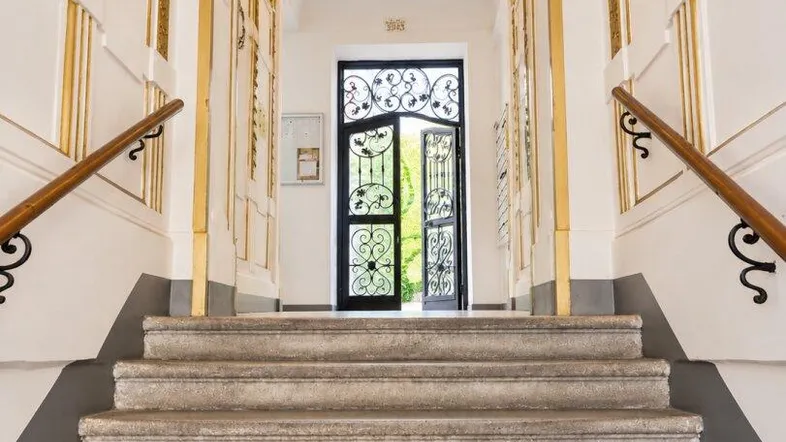 Elegantes Treppenhaus mit Marmorstufen, goldenen Akzenten und einem Kronleuchter im Eingangsbereich.