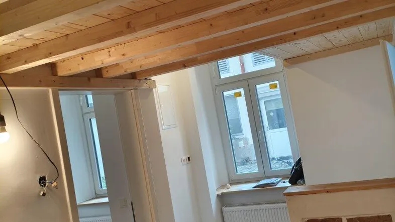 Heller Innenraum mit Holzbalkendecke und Parkettboden, der zu weiteren Zimmern führt.