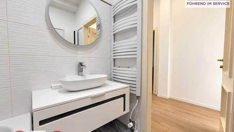 Modernes Badezimmer mit stilvollem Waschtisch, rundem Spiegel und Handtuchheizkörper.