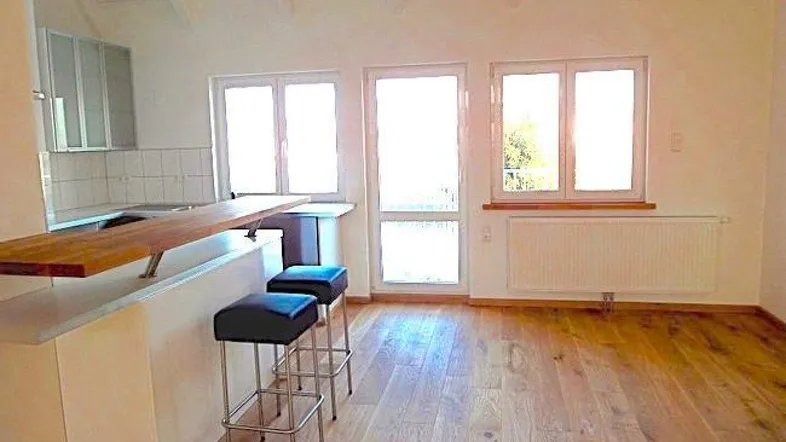 Helle offene Küche mit Holzboden, Frühstücksbar und großen Fenstern, die viel Licht hereinlassen.