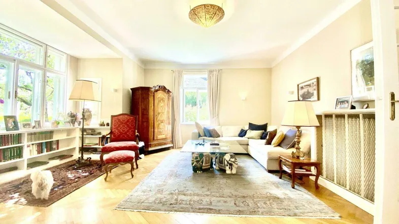 Helles Wohnzimmer mit Parkettboden, großem Sofa, Bücherregalen und viel Tageslicht durch große Fenster.