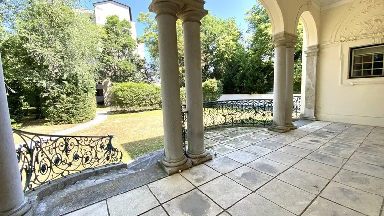 Geräumige überdachte Terrasse mit Säulen, Fliesenboden und Blick auf den gepflegten Garten.