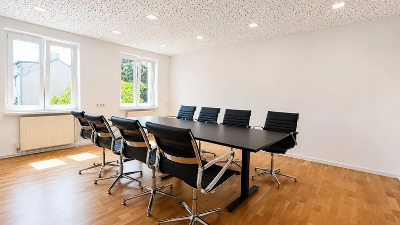 Moderner Konferenzraum mit Holzboden, großen Fenstern und schallabsorbierender Decke.