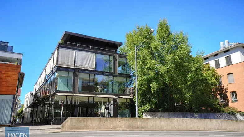 Modernes Geschäftsgebäude mit Glasfassade und viel Grün in der Umgebung unter blauem Himmel.