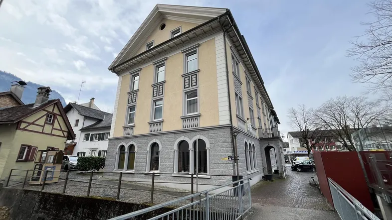 Historisches Gebäude mit gelber Fassade und grauen Steinbögen, umgeben von einer kleinen Brücke.