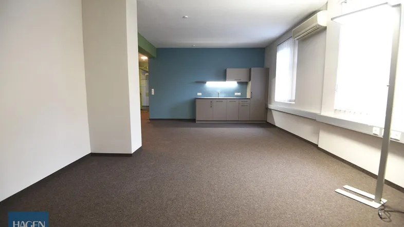 Geräumiger Büroraum mit Teppichboden und integrierter Küchenzeile in modernem Design.