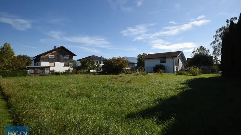 Weitläufiges Grundstück mit grüner Wiese, umgeben von Wohnhäusern und mit Bergblick im Hintergrund.