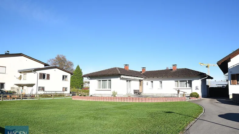 Weißes Einfamilienhaus mit großem Rasen und gepflegtem Vorgarten unter blauem Himmel.