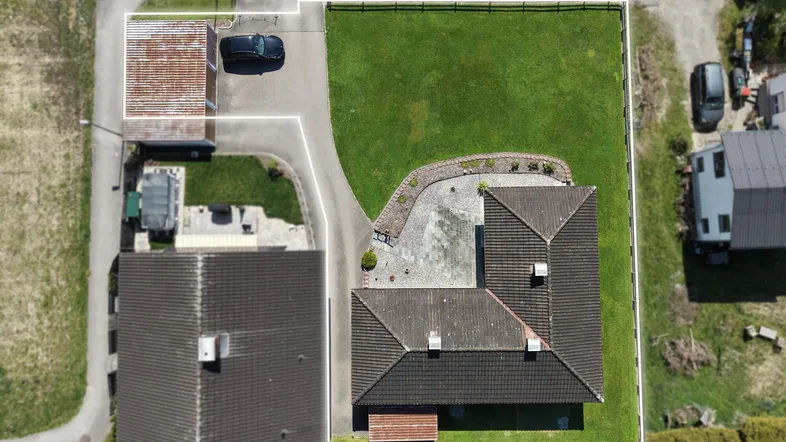 Luftaufnahme eines Einfamilienhauses mit großem Garten, Zufahrt und separater Garage.