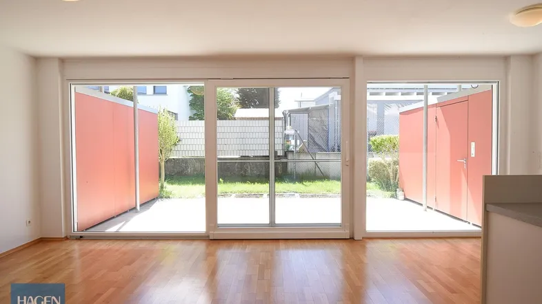 Helles Wohnzimmer mit Holzboden und großen Schiebetüren, die zu einer Terrasse und Gartenfläche führen.