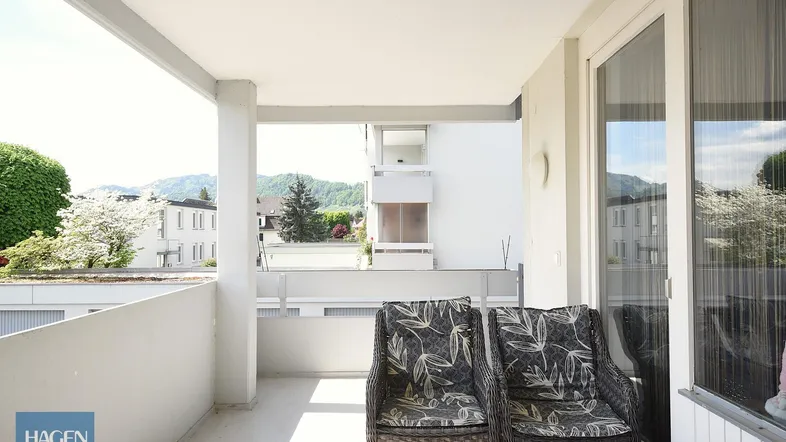 Heller Balkon mit Korbsesseln und Blick auf die umliegende Wohngegend und Berge.