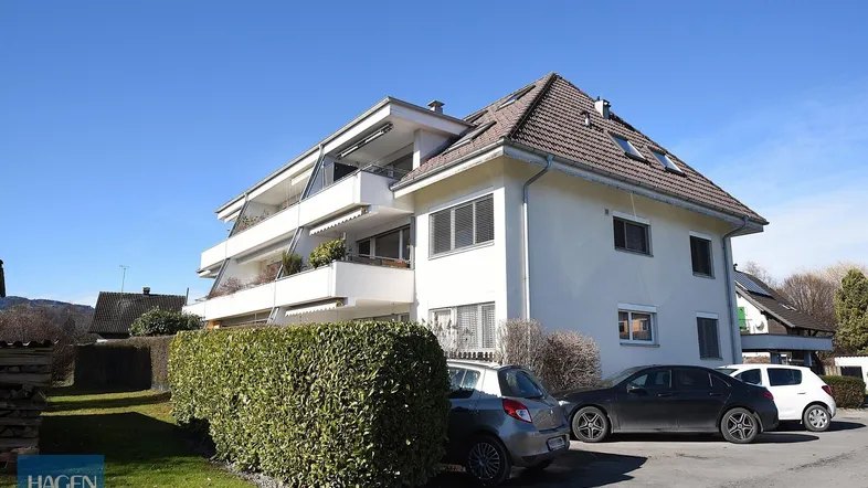 Mehrfamilienhaus mit mehreren Balkonen und Satteldach in sonniger Lage und Parkplätzen.