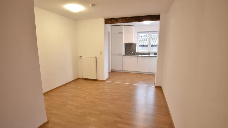 Heller offener Wohnbereich mit Laminatboden, der in eine moderne Küche übergeht.