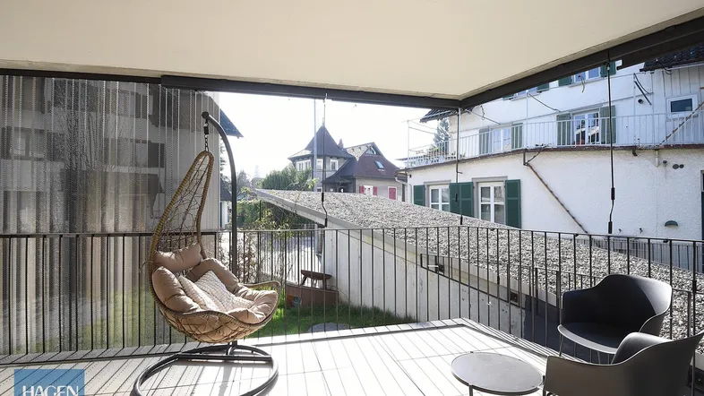 Heller Balkon mit Holzboden, Hängesessel und Blick auf die Umgebung.