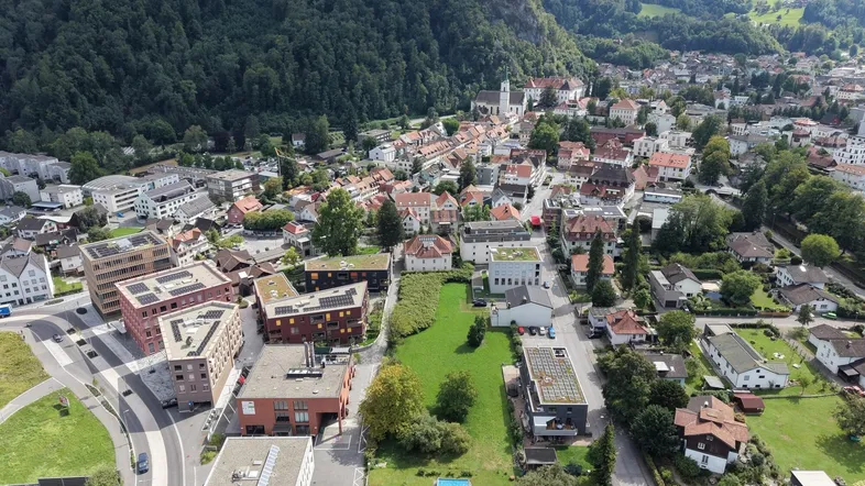 Luftaufnahme einer Stadt in einer Berglandschaft mit Wohngebäuden und viel Grün.