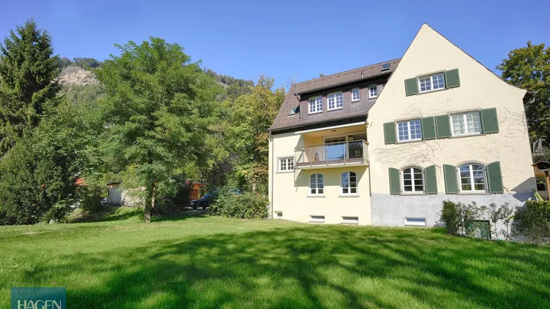 Großzügiges Anwesen mit weitläufigem Garten und traditioneller Architektur unter blauem Himmel.