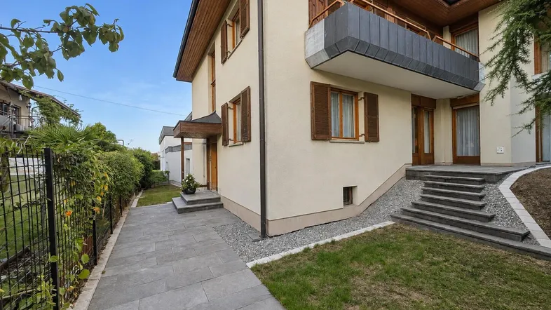 Seitenansicht des Hauses mit gepflegtem Vorgarten, Balkon und Außentreppe.