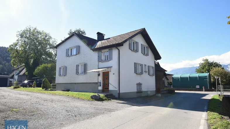 Weißes Wohnhaus mit Satteldach und grauen Fensterläden in ländlicher Umgebung.