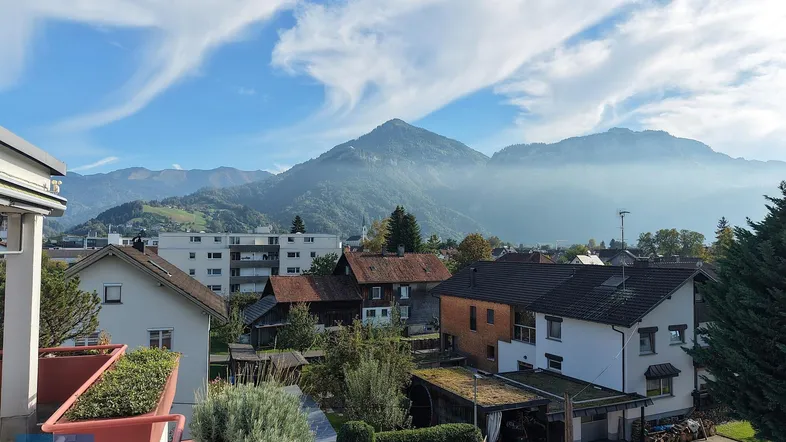 Panoramablick auf die umliegende Berglandschaft und die darunter liegende Siedlung bei sonnigem Wetter.