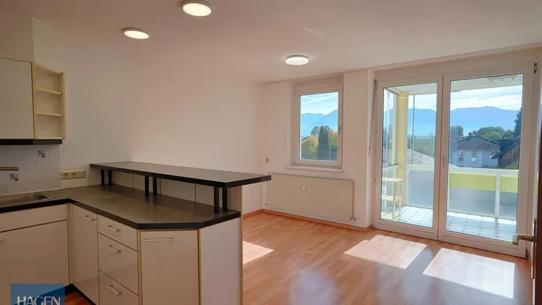 Helles Wohn-Esszimmer mit integrierter Küche, Parkettboden und Zugang zum Wintergarten mit Bergblick.