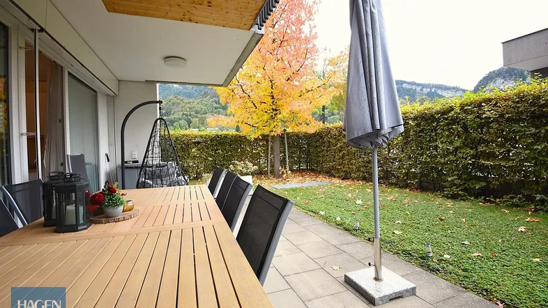 Geräumige Terrasse mit Holztisch, Gartenmöbeln und Blick auf die umliegende Natur und Berge.