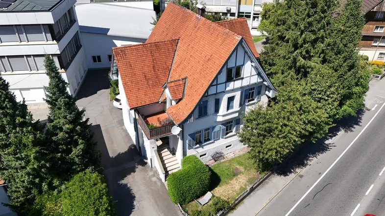 Luftaufnahme eines charmanten Hauses mit rotem Ziegeldach und umliegender Bebauung.