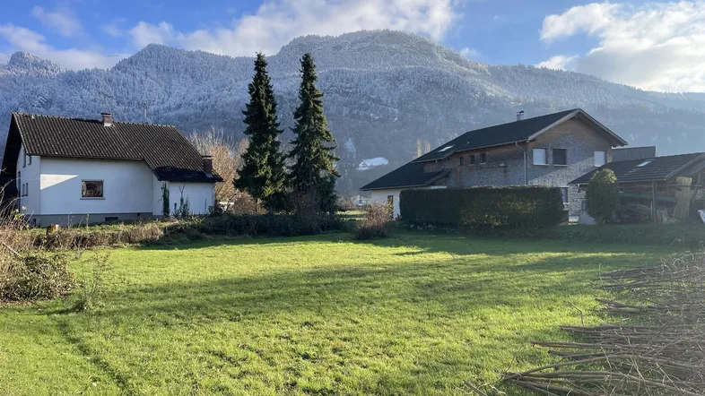 Weitläufiges Grundstück mit grüner Wiese und Blick auf schneebedeckte Berge im Hintergrund.