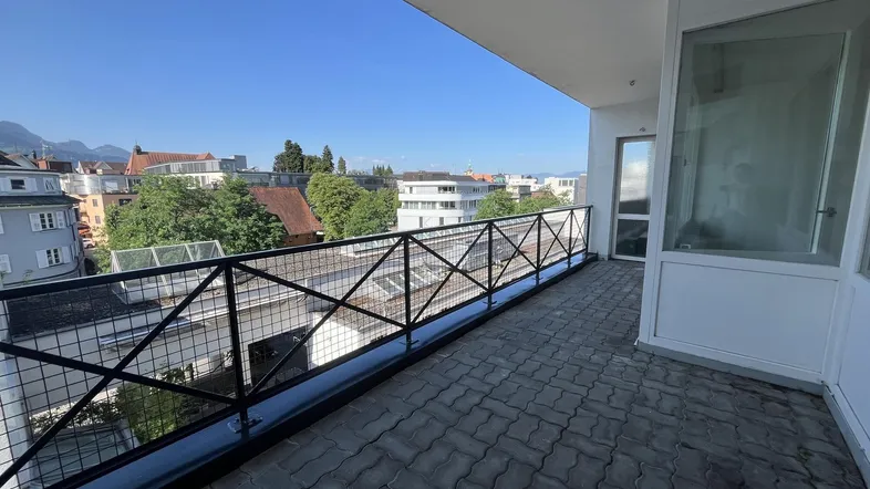 Langer Balkon mit gepflastertem Boden und weitem Blick über die Stadt und Berge.