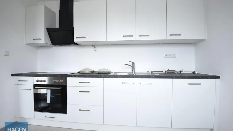 Moderne Einbauküche in Weiß mit dunkler Arbeitsplatte, ausgestattet mit Backofen und Induktionskochfeld.