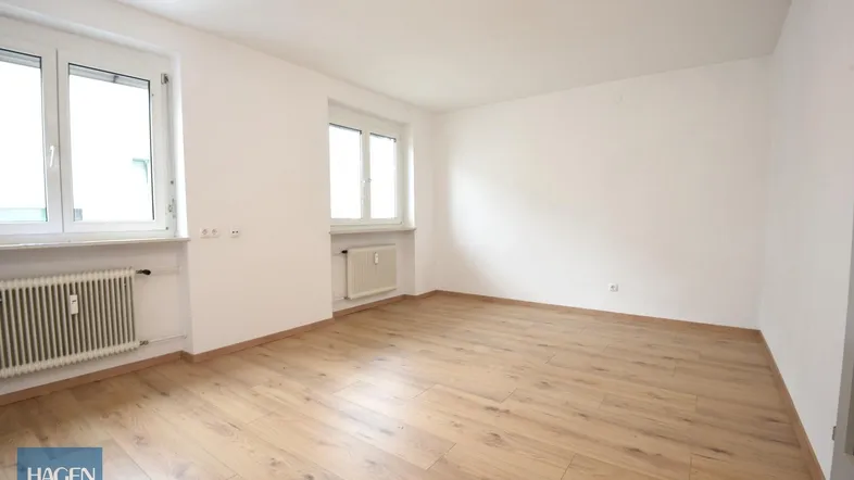 Helles Zimmer mit Laminatboden und zwei Fenstern, bereit zur individuellen Gestaltung.