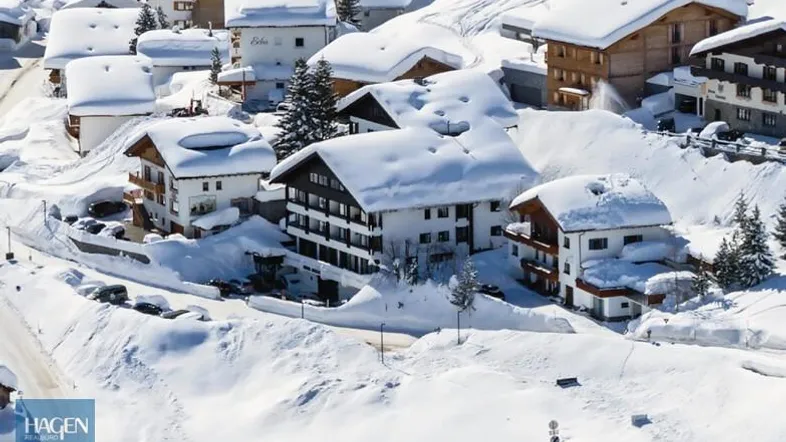 Winterliche Luftaufnahme eines verschneiten Bergdorfes mit traditionellen Häusern und Pisten.