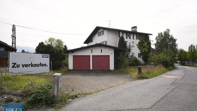 Vorderansicht des Hauses mit Doppelgarage und einem "Zu verkaufen"-Schild an der Straße.