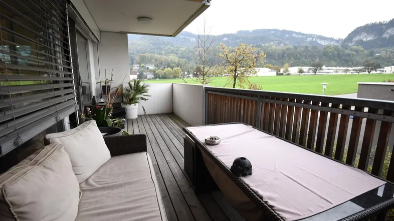 Geräumiger Balkon mit Holzboden, Sitzgelegenheiten und weitem Blick ins Grüne und auf die Berge.