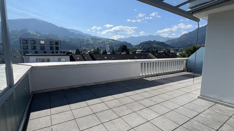 Große Dachterrasse mit Fliesenboden und weitem Blick auf die umliegende Berglandschaft unter klarem Himmel.
