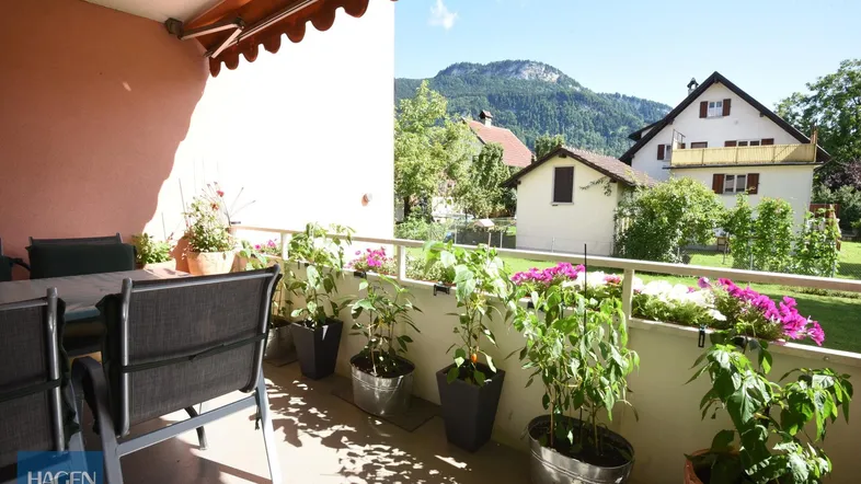Sonniger Balkon mit Gartenmöbeln, Pflanzen und Bergblick in ruhiger Umgebung.