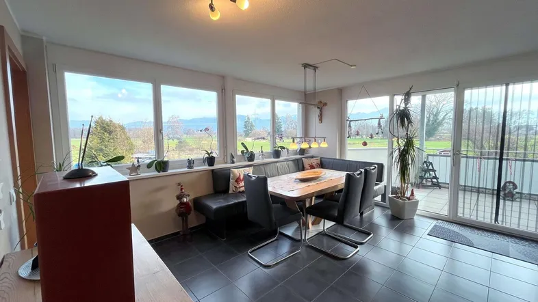 Geräumiger Wohn-Essbereich mit großen Fenstern, Fliesenboden und Zugang zum Balkon mit Weitblick.