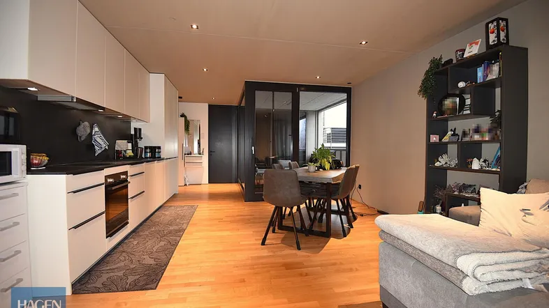 Geräumiger offener Wohn-Essbereich mit integrierter Küche, Holzboden und Zugang zum Balkon.