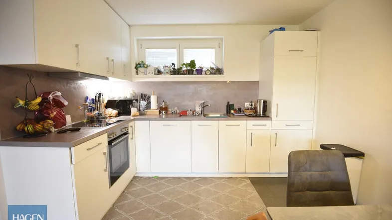 Helle Küche mit weißen Schränken, integriertem Backofen und Fenster über der Spüle.