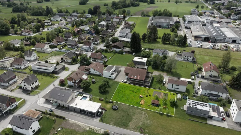 Luftaufnahme eines Wohngebiets mit grünen Feldern und Bergen im Hintergrund, die das Grundstück umgeben.