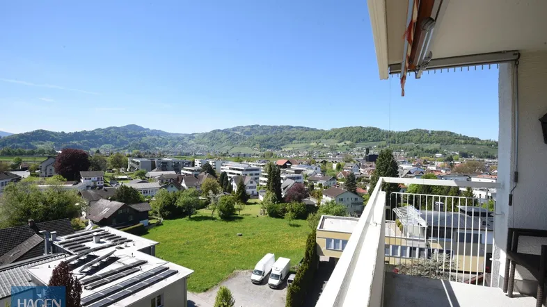 Geräumiger Balkon mit Markise und weitem Blick über die Stadt und die umliegenden Berge.